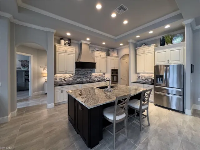 Kitchen with large island - granite countertops, stainless steel appliances, a center island with sink, custom range hood, and sink
