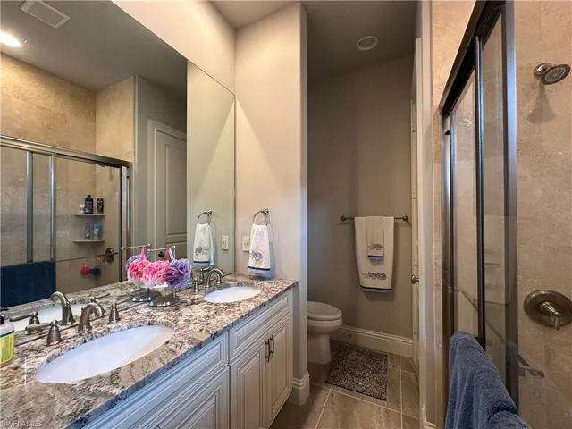 Bathroom featuring toilet, tile flooring, a shower with shower door, and vanity with double sinks