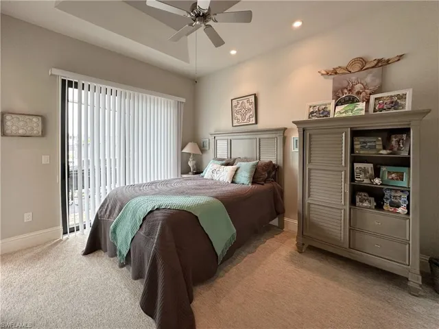 Carpeted bedroom featuring ceiling fan, access to lanai, and a tray ceiling