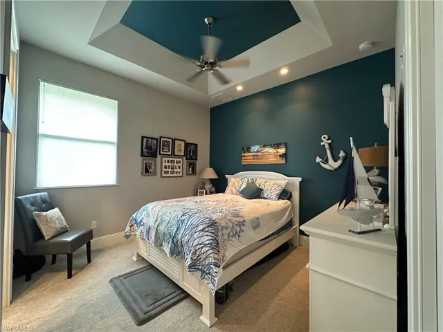 Bedroom with ceiling fan, a tray ceiling, and light carpet