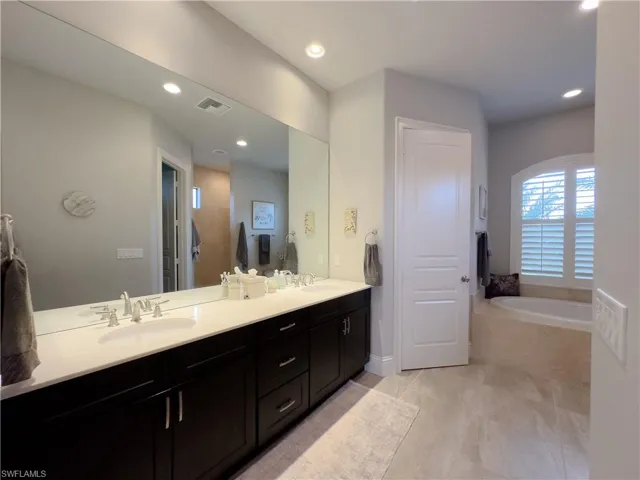 Primary Bathroom with double sinks with a relaxing tub, tile floors