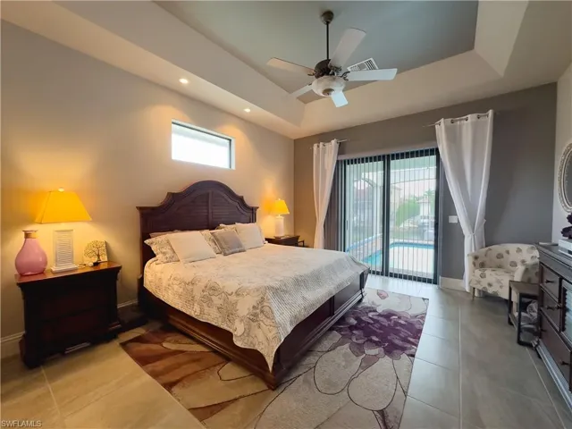 Primary bedroom with sliders access to lanai & pool, ceiling fan, and a tray ceiling