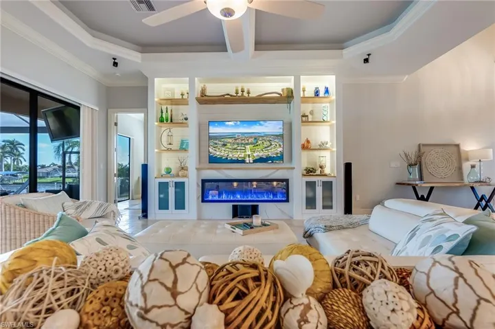 Tiled living room with a premium fireplace, beamed ceiling, ceiling fan, and crown molding