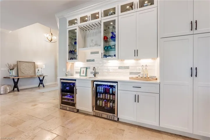 Bar with wine cooler, tasteful backsplash, hanging light fixtures, and white cabinets