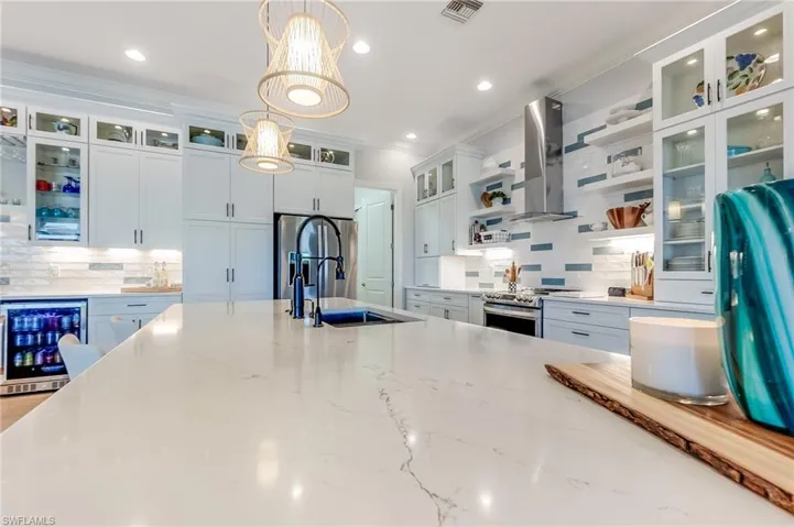 Kitchen with stainless steel appliances, wine cooler, light stone counters, wall chimney exhaust hood, and hanging light fixtures