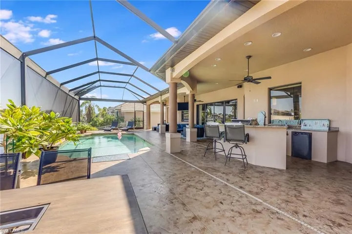 View of pool with glass enclosure, a patio, an outdoor bar, area for grilling, and ceiling fan