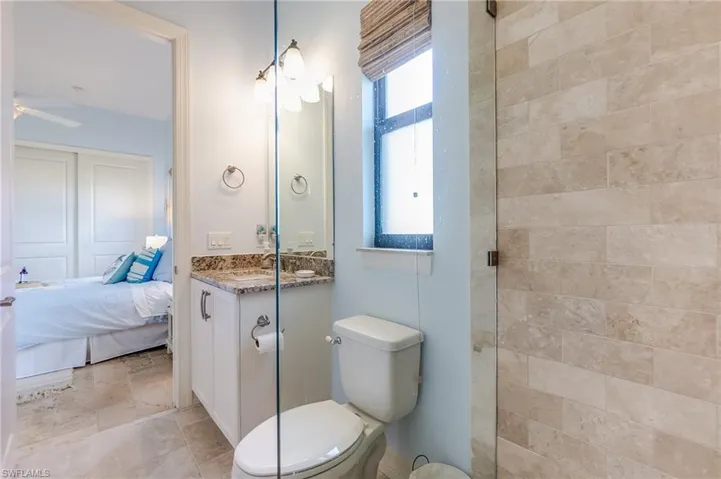 Bathroom featuring tiled shower, vanity, ceiling fan, and toilet