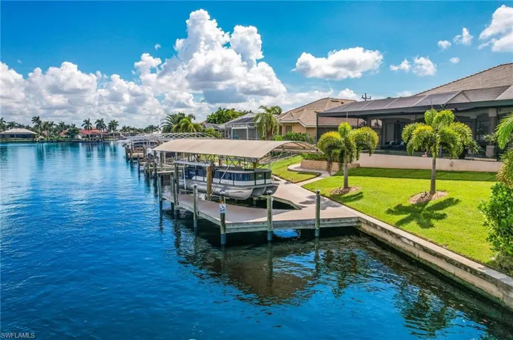 View of dock with a lanai, a yard, and a water view