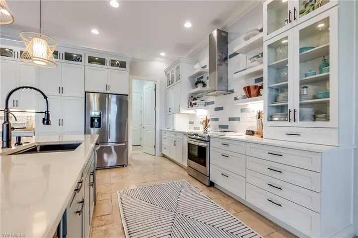 Kitchen featuring white cabinets, hanging light fixtures, sink, extractor fan, and appliances with stainless steel finishes