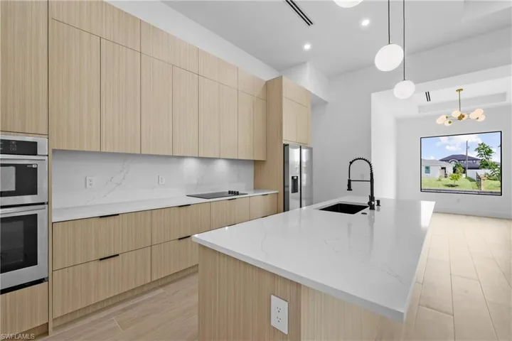 Kitchen with modern cabinets, light brown cabinetry, appliances with stainless steel finishes, wood finish floors, and a center island with sink