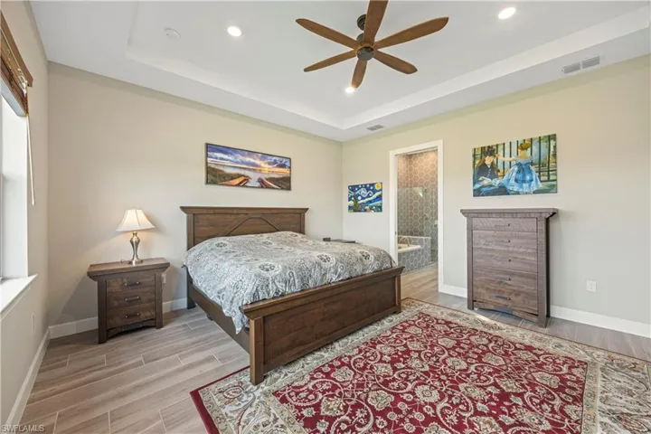 Bedroom with wood tiled floors, ceiling fan, a raised ceiling, recessed lighting, and connected bathroom