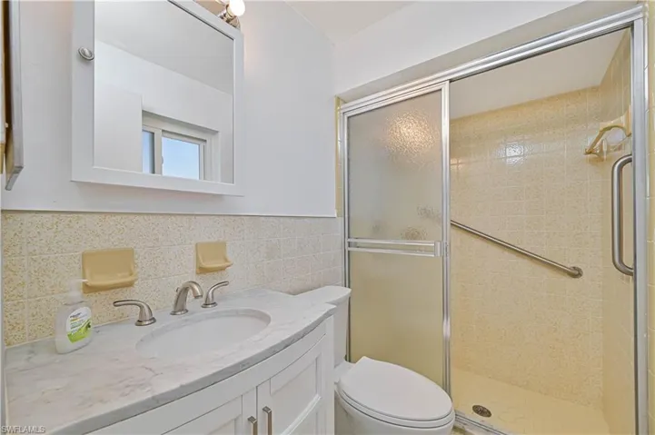 Primary Full bathroom featuring a wainscoted wall, toilet, tile walls, a shower stall, and vanity
