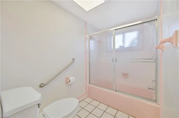 Bathroom with tile patterned floors, toilet, baseboards, and bath / shower combo with glass door