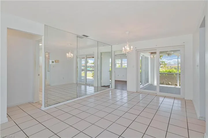 Empty room featuring light tile patterned flooring, visible vents, and ceiling fan with notable chandelier and wall mirrors