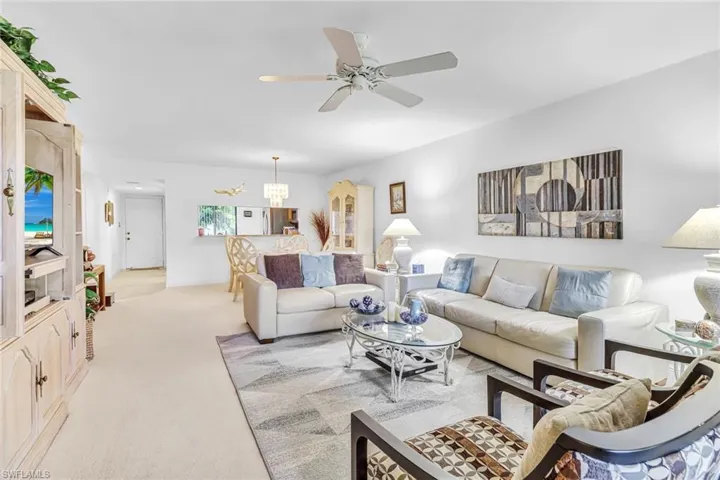 Living room featuring ceiling fan with notable chandelier and light colored carpet