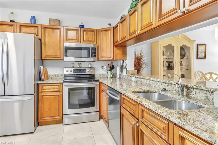 Kitchen with sink, appliances with stainless steel finishes, light stone counters, and light tile patterned floors
