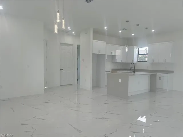 Kitchen with decorative light fixtures, light tile patterned flooring, white cabinets, and a kitchen island with sink