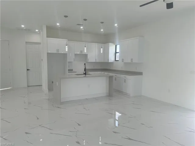 Kitchen with light tile patterned floors, sink, ceiling fan, white cabinetry, and a center island with sink