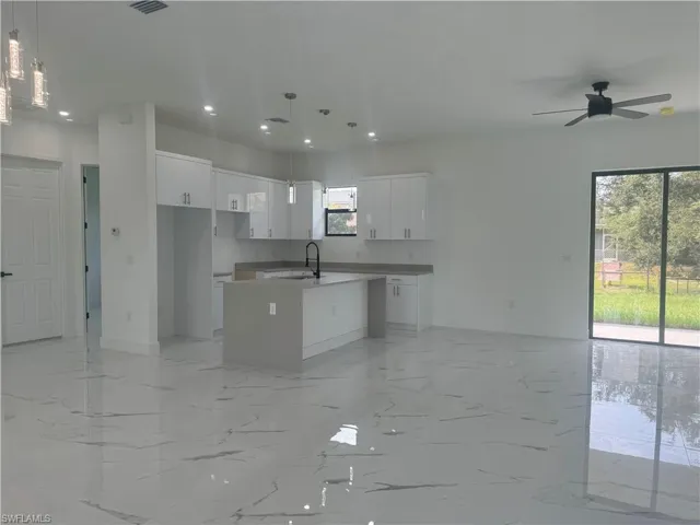 Kitchen with hanging light fixtures, white cabinetry, an island with sink, and plenty of natural light