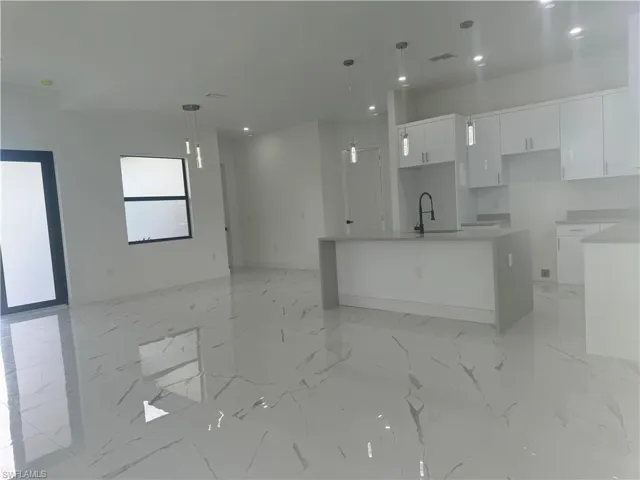 Kitchen featuring a center island with sink, pendant lighting, light tile patterned flooring, and white cabinets