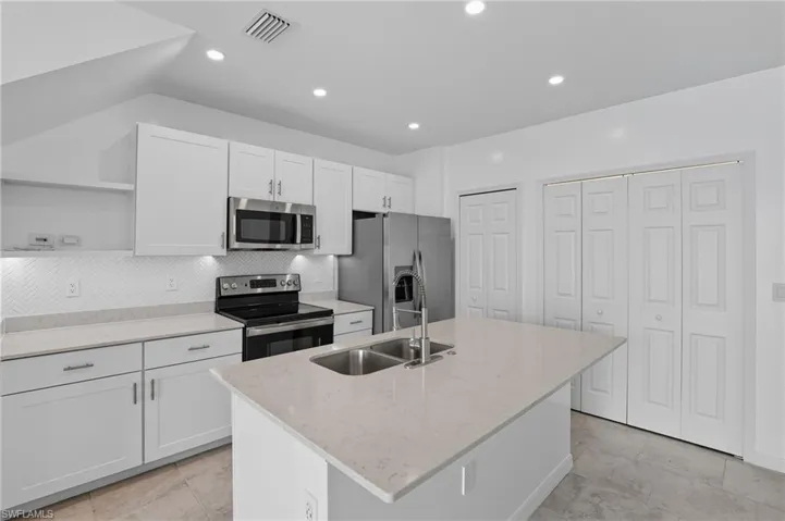 Kitchen with white cabinetry, stainless steel appliances, light stone counters, a kitchen island with sink, and open shelves