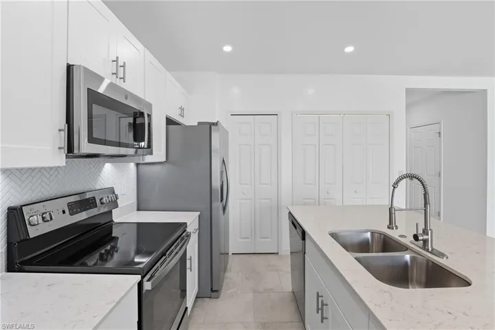 Kitchen with stainless steel appliances, white cabinetry, light stone counters, recessed lighting, and tasteful backsplash