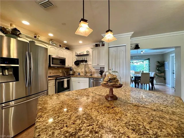 Kitchen with white cabinetry, tasteful backsplash, hardwood / wood-style floors, appliances with stainless steel finishes, and pendant lighting