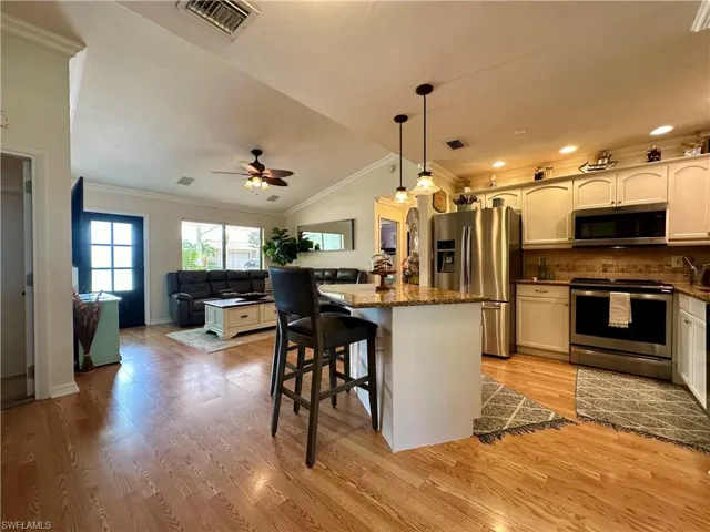 Kitchen with appliances with stainless steel finishes, light wood-type flooring, lofted ceiling, ceiling fan, and ornamental molding