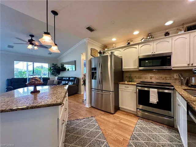 Kitchen with light hardwood / wood-style flooring, stainless steel appliances, hanging light fixtures, crown molding, and ceiling fan