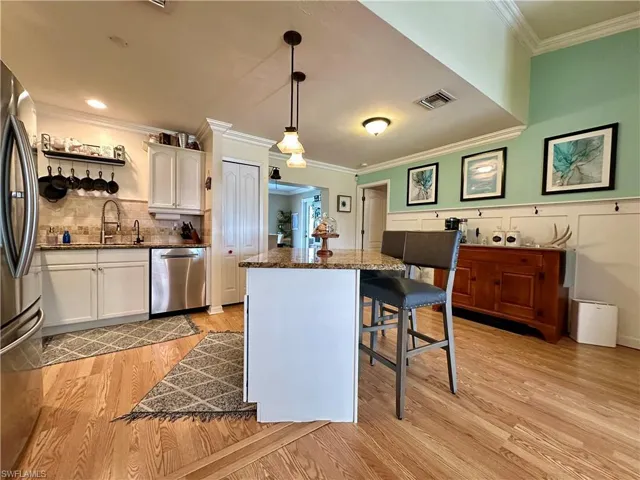 Kitchen featuring light hardwood / wood-style flooring, stainless steel appliances, decorative light fixtures, a kitchen island, and white cabinetry