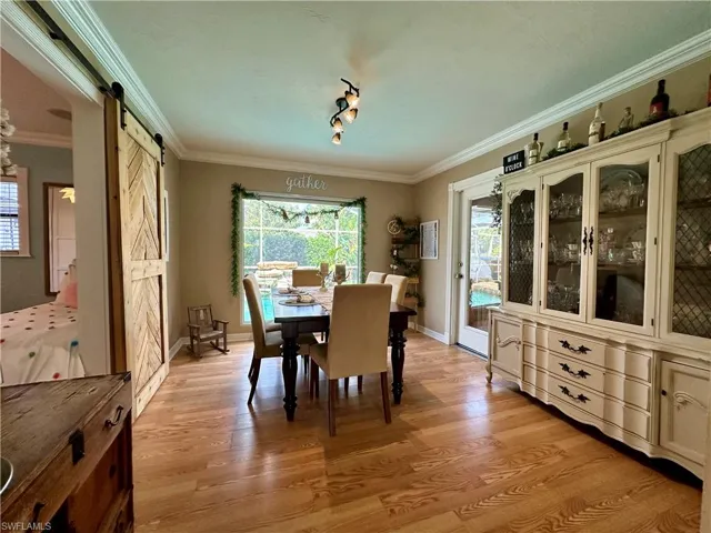 Dining room with light hardwood / wood-style floors, ornamental molding, and a barn door