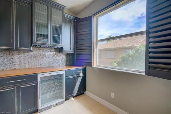 Kitchen featuring tasteful backsplash, vaulted ceiling, light tile patterned floors, and beverage cooler
