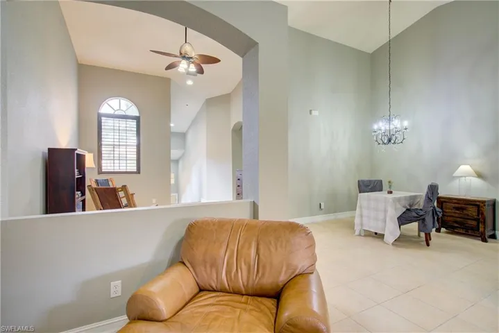 Living area featuring light tile patterned floors, ceiling fan with notable chandelier, and vaulted ceiling