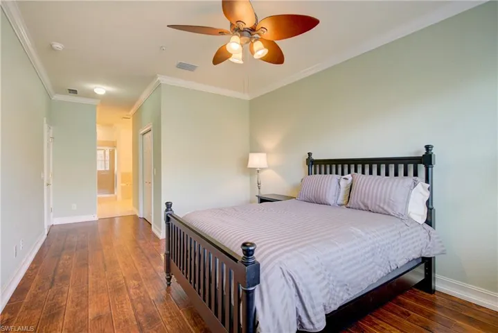 Bedroom featuring dark hardwood / wood-style flooring, crown molding, connected bathroom, and ceiling fan