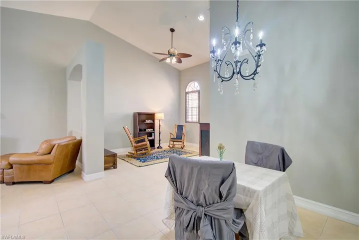 Tiled dining area with vaulted ceiling and ceiling fan with notable chandelier