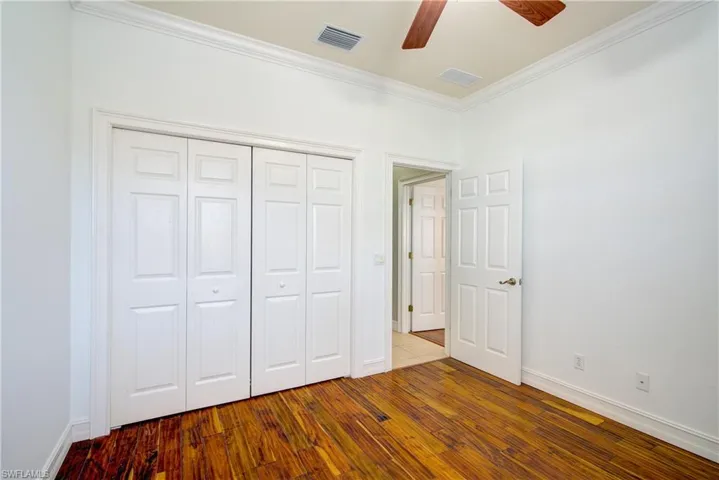 Unfurnished bedroom with hardwood / wood-style flooring, ceiling fan, crown molding, and a closet