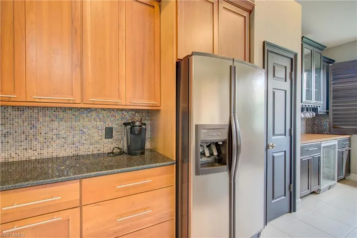 Kitchen with light tile patterned floors, decorative backsplash, dark stone counters, and stainless steel refrigerator with ice dispenser