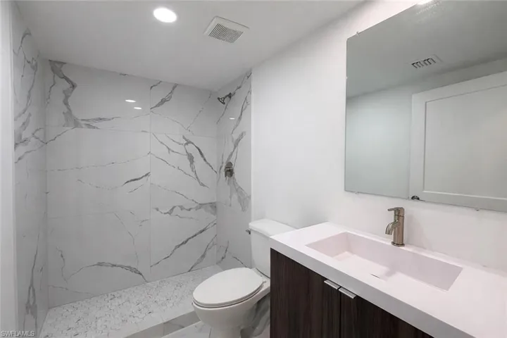 Bathroom with a marble finish shower, vanity, and recessed lighting