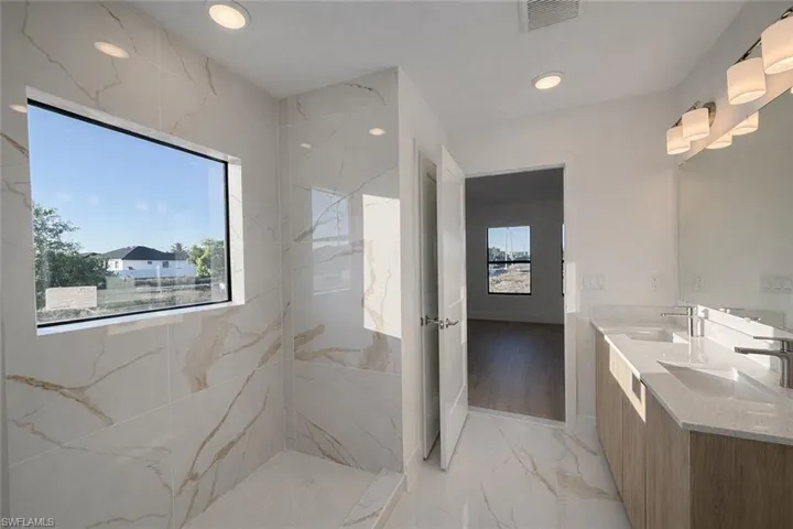 Bathroom with double vanity, light marble finish flooring, recessed lighting, and a marble finish shower