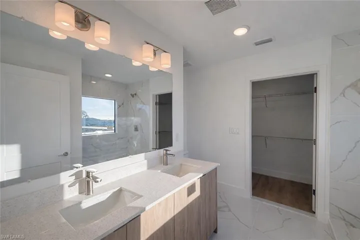 Bathroom with a marble finish shower, a walk in closet, double vanity, and light marble finish flooring