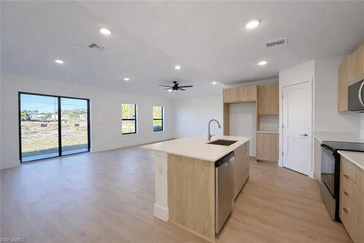 Kitchen featuring stainless steel appliances, a kitchen island with sink, open floor plan, light stone countertops, and modern cabinets