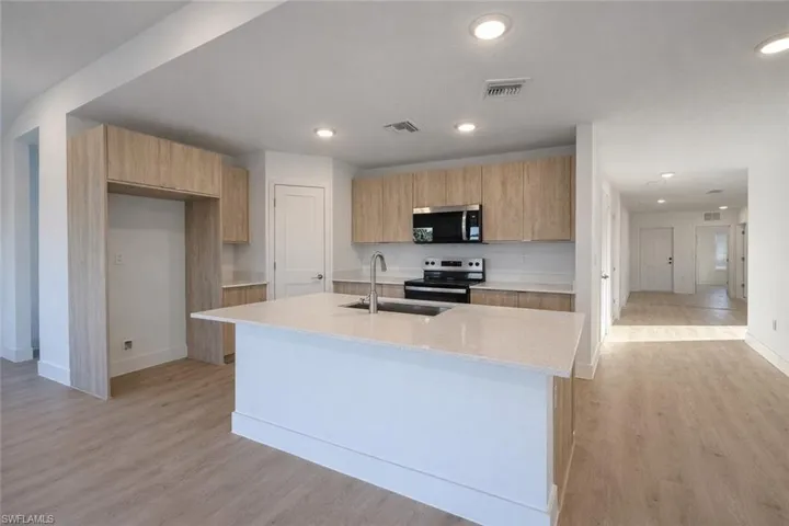 Kitchen with modern cabinets, stainless steel appliances, light stone countertops, light wood-type flooring, and recessed lighting