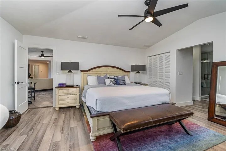 Spacious bedroom featuring vaulted ceilings, wood-finish flooring, a contemporary ceiling fan, and louvered bifold closet doors
