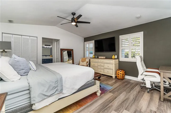Vaulted ceilings with a ceiling fan, plank-style flooring, white louvered bifold closet doors, and plantation shutters