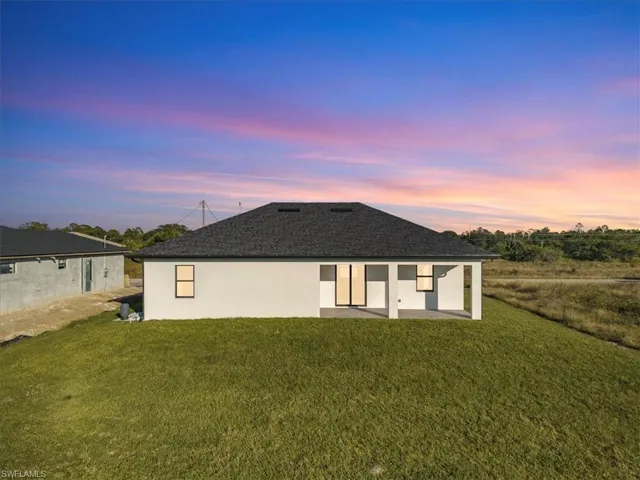 Back of property at dusk featuring a patio area, a yard, stucco siding, and roof with shingles