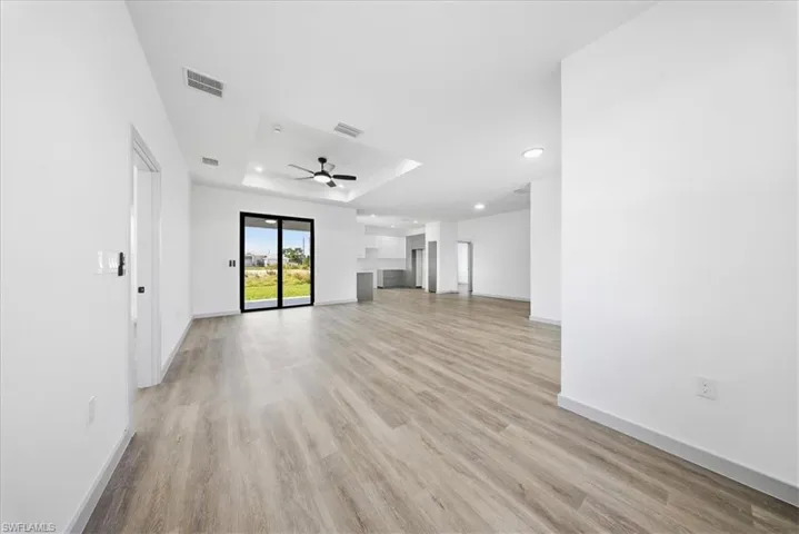 Unfurnished living room featuring light wood-style flooring, recessed lighting, a tray ceiling, and ceiling fan