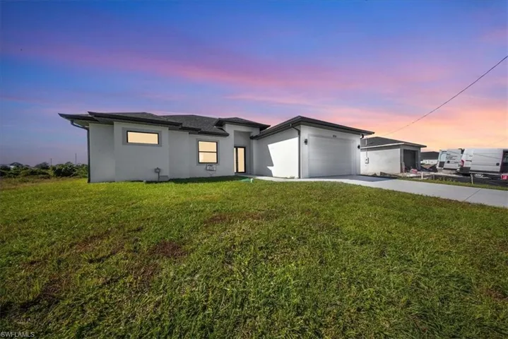 Prairie-style home featuring concrete driveway, stucco siding, an attached garage, and a front lawn
