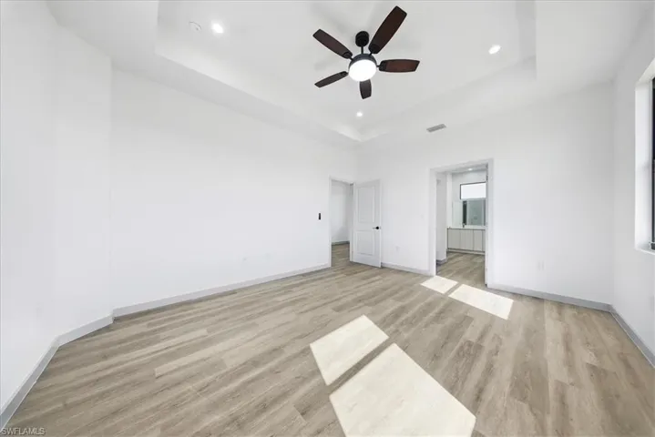 Unfurnished bedroom featuring a tray ceiling, light wood finished floors, ceiling fan, and recessed lighting