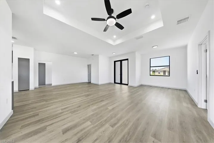 Unfurnished living room with a raised ceiling, light wood-style flooring, recessed lighting, and a ceiling fan