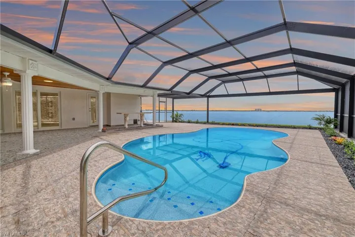 Pool at dusk with glass enclosure, ceiling fan, a water view, and a patio